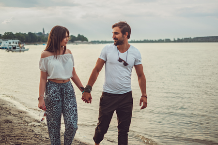 Smiling couple holding hands and looking at each other while walking on the beachの写真素材