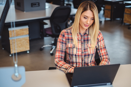 Blonde woman working on a laptop in office and smilingの写真素材