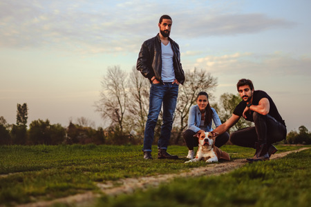 Friends standing in the meadow road with their dogの写真素材