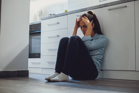 Depressed woman sitting on a kitchen floor and holding her headの写真素材
