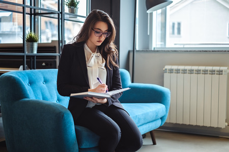 Beautiful businesswoman siting in the office resting area and writing in her notebookの写真素材