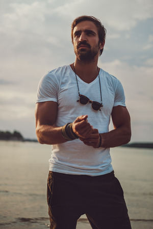 Muscular bearded guy standing by the river in the sunsetの写真素材