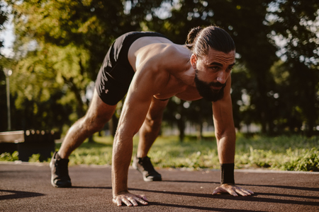 Bearded man doing dive bomber push ups in the outdoor gym on a sunny dayの写真素材