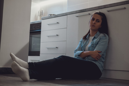 Depressed girl sitting on the kitchen floor with her arms crossedの写真素材