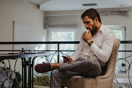 Man looking at mobile phone and smoking electronic cigarette in a cafeの写真素材