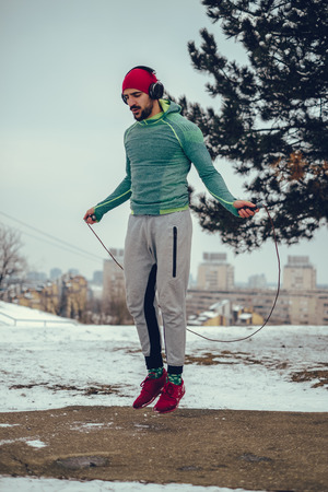Muscular focused man jumping rope outside on a winter day with headphones on his headの写真素材