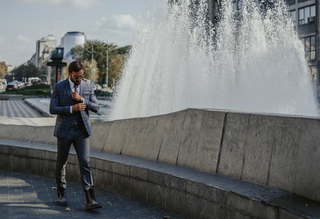 Businessman walking by the fountain in the city and fixing his cuffsの写真素材