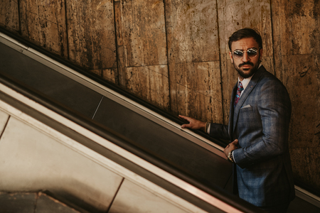 Serious businessman going up on the escalator while holding jacket on a sunny day