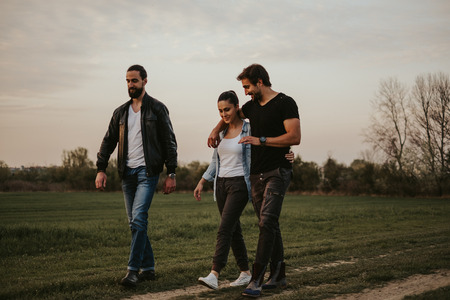 Couple walking with friend in nature and talking. Sunset