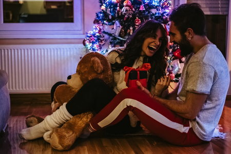 Man giving present to his girlfriend in front of Christmas treeの写真素材