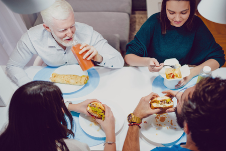 Friends smiling while eating fast food for a diner in the houseの写真素材