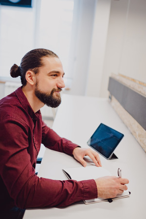 Smiling man with beard and man bun working in the officeの写真素材