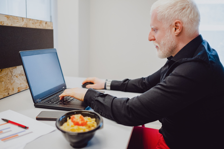 Serious senior man with white hair and beard working on a laptop  in the officeの写真素材