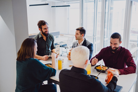 Smiling coworkers having lunch at the table in the officeの写真素材