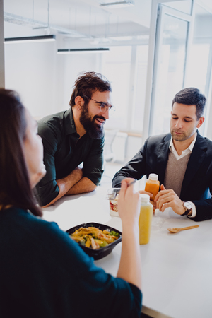 Man with beard smiling in the office cafeteria while colleagues eatingの写真素材