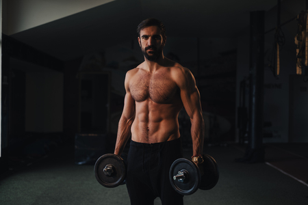Shirtless athlete man with beard holding dumbbells in the gymの写真素材