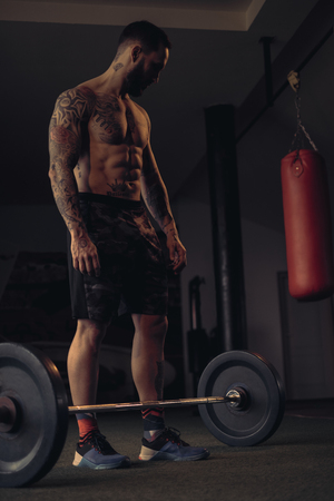 Shirtless, tattooed,bearded athlete lpreparing to lift weights from the gym floorの写真素材