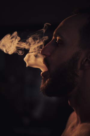 Serious man with beard exhaling smokeの写真素材