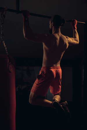 Shirtless boxer with beard doing pull ups on the bar in the gymの写真素材
