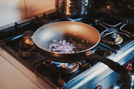 Onions cooking in oil in the frying pan on the gas stoveの写真素材