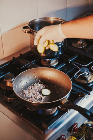 Kitchen chef dropping sliced cucumber in to a frying pan on the gas stoveの写真素材