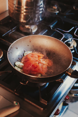 Tomato and cucumber cooking in oil in the frying pan on the gas stoveの写真素材