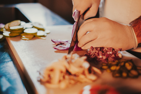 Chef cutting onion with a knife on the board while wearing glovesの写真素材