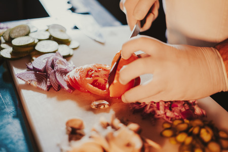 Kitchen chef cutting fresh tomato with a knife on the cutting boardの写真素材