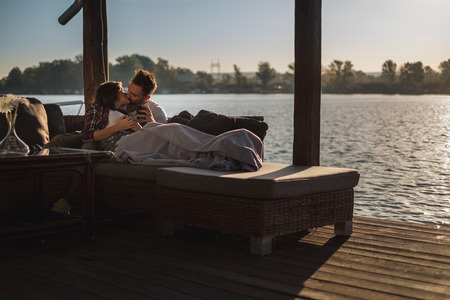 Couple lying under the blanket and kissing by the river ona sunny dayの写真素材