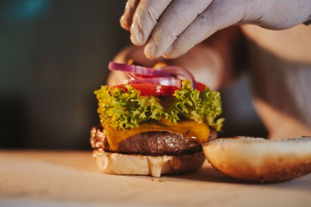 Kitchen chef assembling cheeseburger by adding onion with gloves onの写真素材