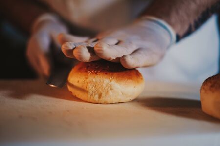 Kitchen chef start cutting hamburger bun with a knife and gloves on