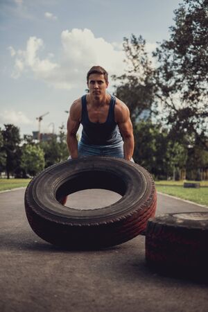 Concentrated athletic man flipping tire in the outdoor gymの写真素材