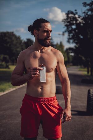 Shirtless hipster man eating protein bar after hard workoutの写真素材