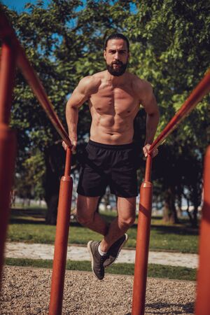 Bearded man doing dips in the park and looking in to the cameraの写真素材
