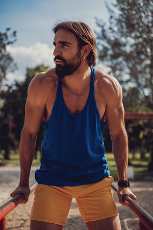 Handsome athlete doing dips on the bars in the outdoor gymの写真素材