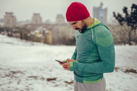 Male athlete using mobile phone outside on a cold winter dayの写真素材
