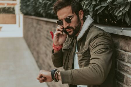 Angry, bearded man checking the time while talking on the phoneの写真素材