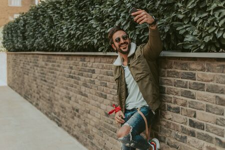Happy, bearded man taking a selfie with his mobile phone while leaning on the wallの写真素材