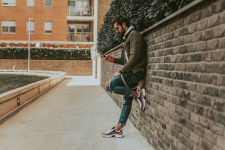 Serious , urban man looking at mobile phone while waiting leaned on the wallの写真素材