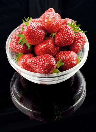 Strawberries in a glass bowl on glossy black backgroundの写真素材