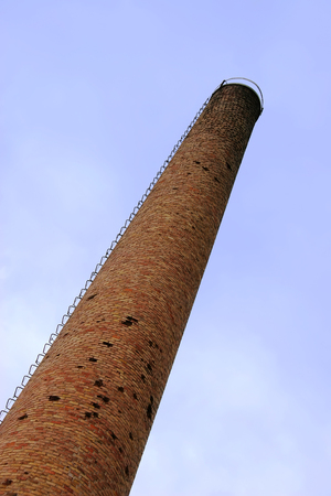Old weathered tall industrial factory chimney, red grungy brick smokestack perspectiveの写真素材