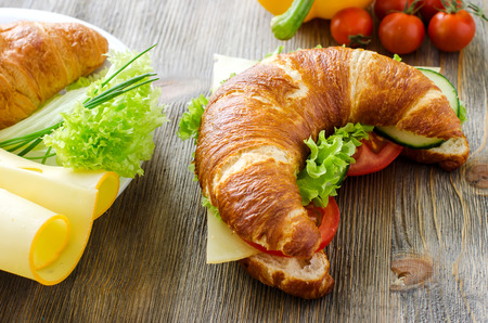 Croissant sandwich with cheese and vegetables for healthy snack, rustic wooden backgroundの写真素材