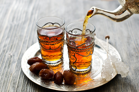 Tea pouring into glass from metal teapotの写真素材