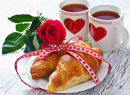 Romantic breakfast with tea in cups, croissants and roseの写真素材