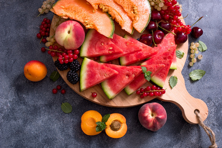 Fresh summer fruits and berries on a round cutting board, watermelon, cantaloupe, cherries, vegan raw eating, diet vitamins conceptの写真素材