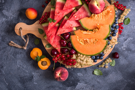 Fresh summer fruits and berries on a round cutting board, watermelon, cantaloupe, cherries, vegan raw eating, diet vitamins conceptの写真素材