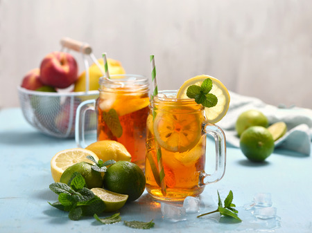 Iced tea with lemons, limes and mint with ice cubes, summer refreshment drink, cold fruit tea,  blue backgroundの写真素材