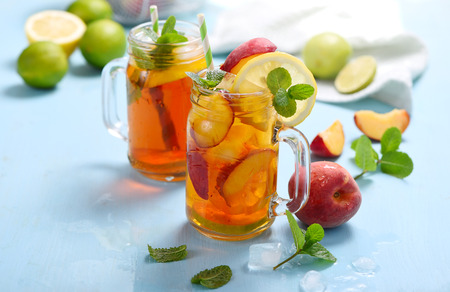 Iced tea with peaches, lemons, limes and mint with ice cubes, summer refreshment drink, cold fruit tea,  blue backgroundの写真素材