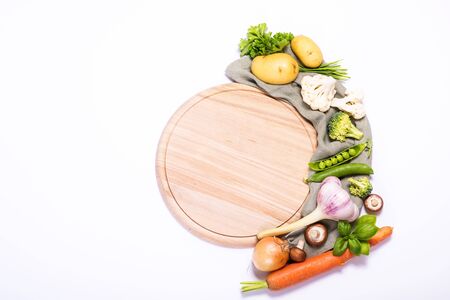 Fresh vegetables for cooking around round empty cutting board, ingredients for healthy eating, copy space white background, place for text, vegan and vegetarian food, recipe and cooking conceptの写真素材