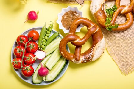 Pretzels and vegetables on yellow background, german traditional food, bavarian snack, european breakfast, oktoberfest conceptの写真素材